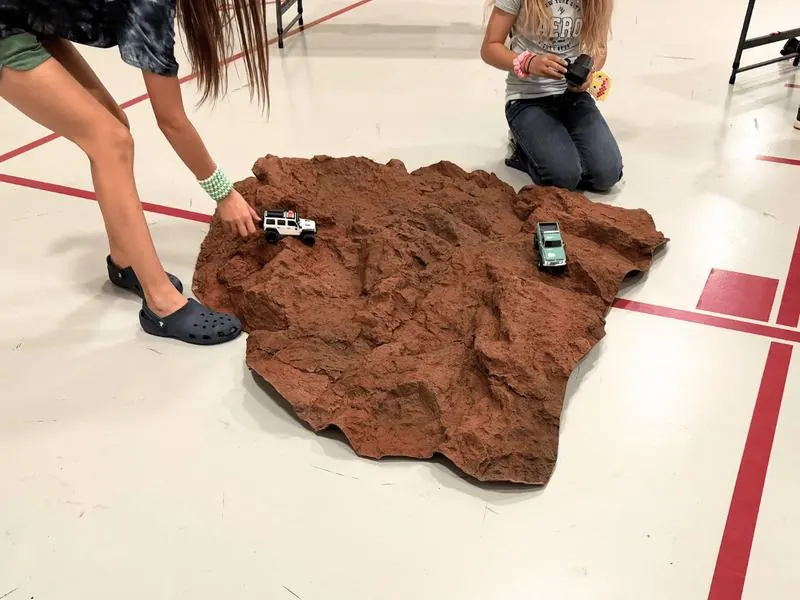 Two kids at a rock terrain course with a white and a teal RC truck